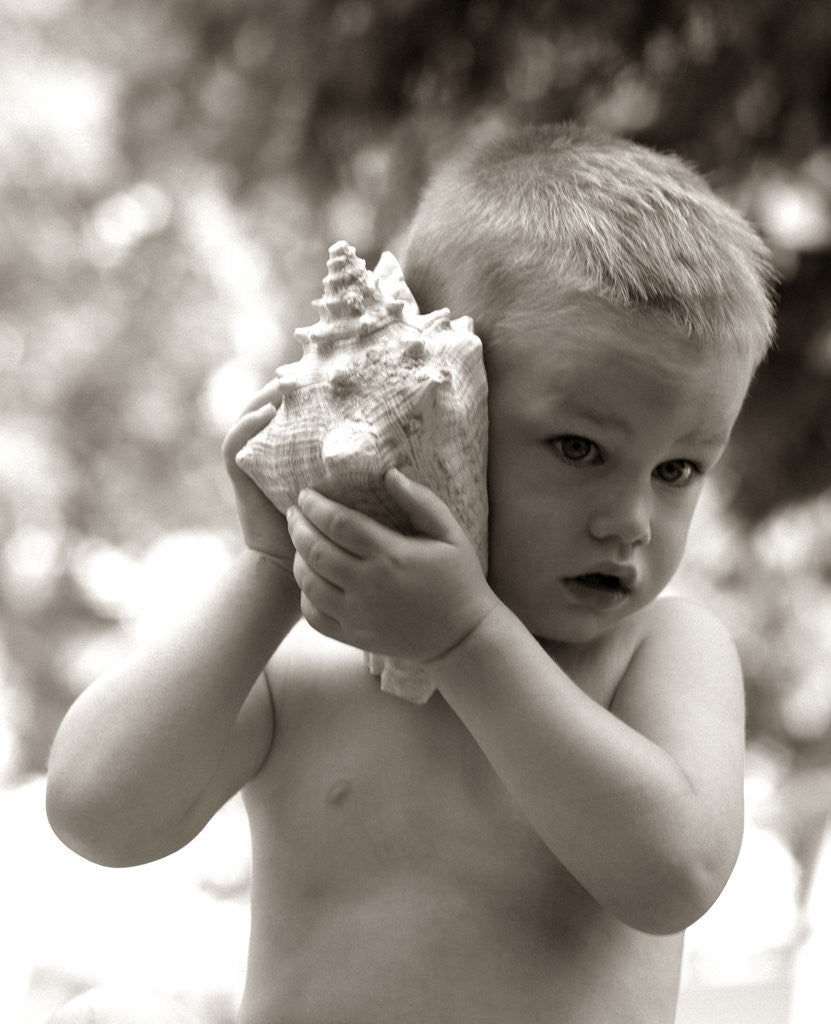 Detail of 1960s Boy Toddler Holding Seashell To Ear Listening To Ocean Sounds Summer Beach by Corbis