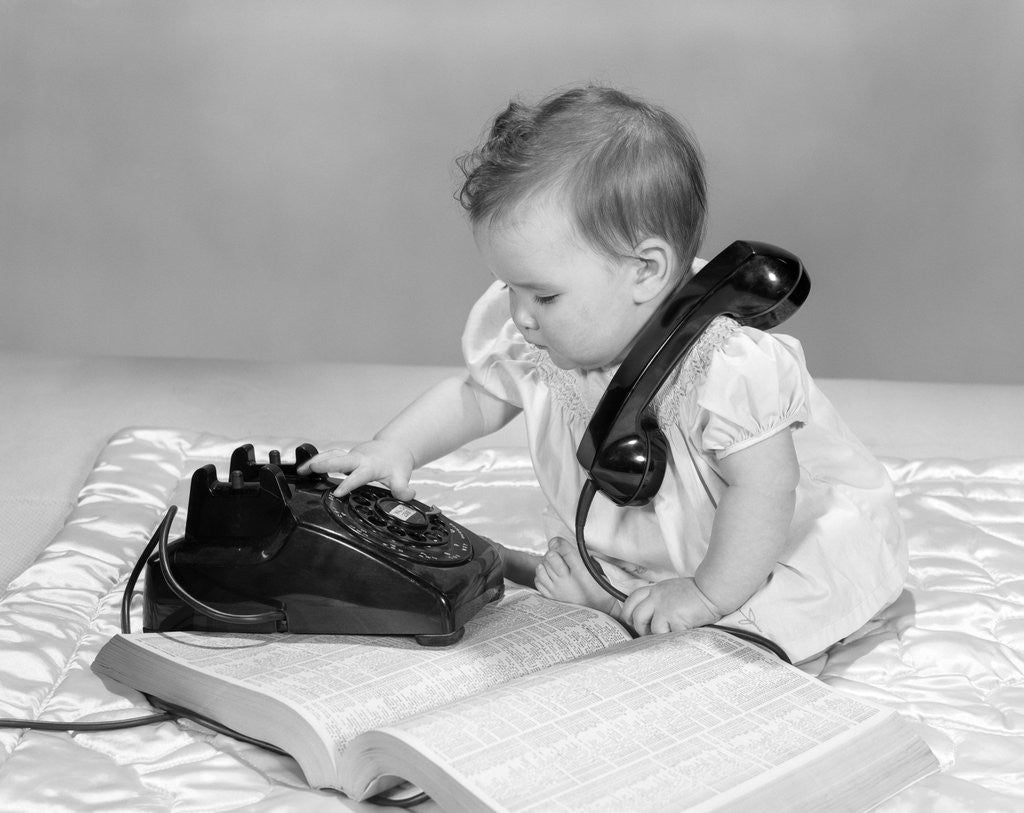 Detail of 1950s 1960s Baby Girl With Telephone Book Dialing Phone by Corbis