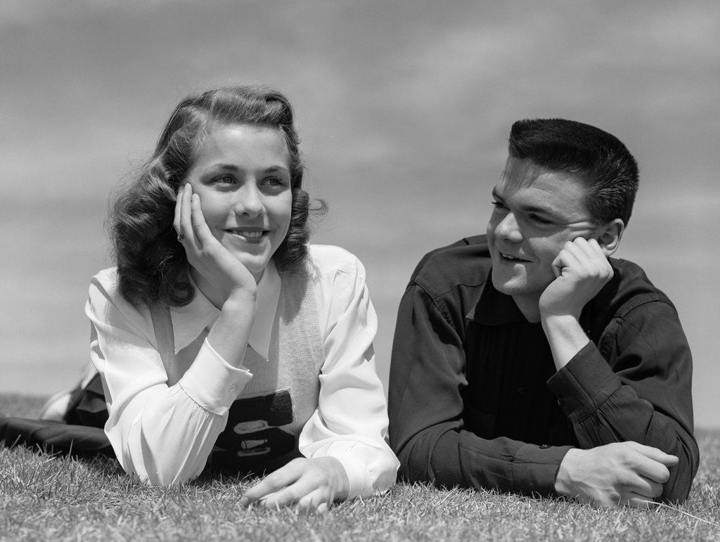 Detail of 1950s Teenage Couple Laying On Grass, Boy Gazing At Girl Wearing Cheerleader Sweater by Corbis