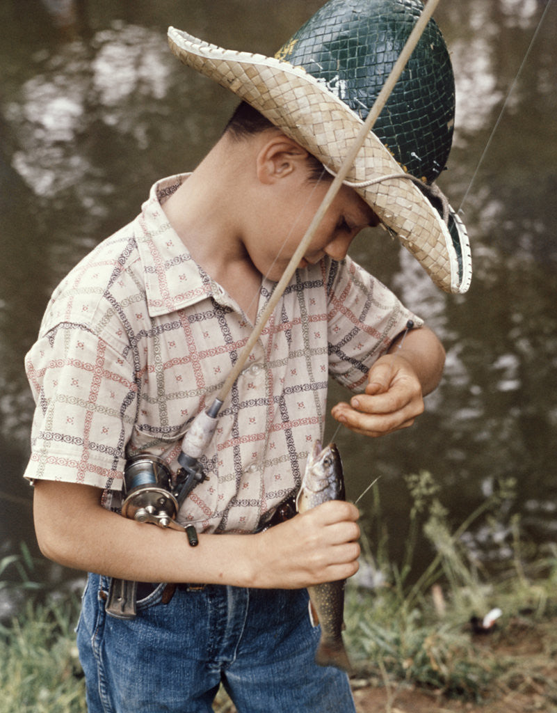 Boy Wearing Straw Hat Removing Hook From Mouth Of Fish Outdoor