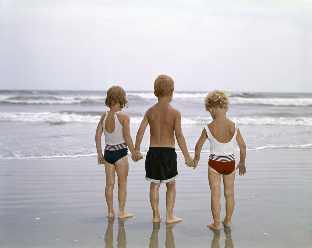 Detail of 1960s Young Children In Bathing Suits Holding Hands On The Beach Looking At The Ocean Waves by Corbis