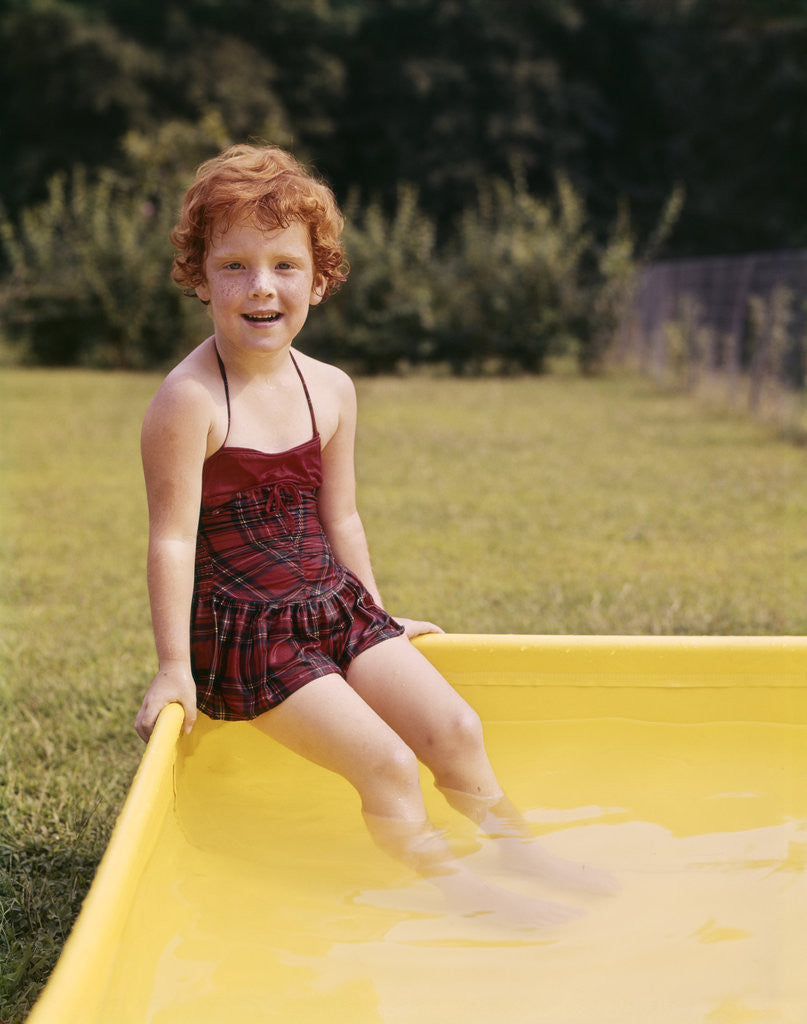 Detail of 1960s Red Haired Little Girl In Plaid Bathing Suit Sitting On Yellow Plastic Backyard Swimming Pool by Corbis