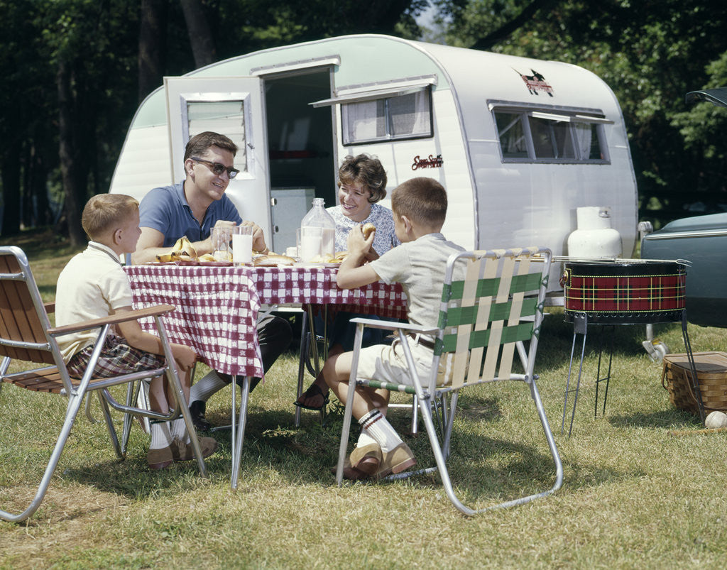 Detail of 1960s Family Sitting In Lawn Chairs At Picnic Table Beside Camping Trailer by Corbis