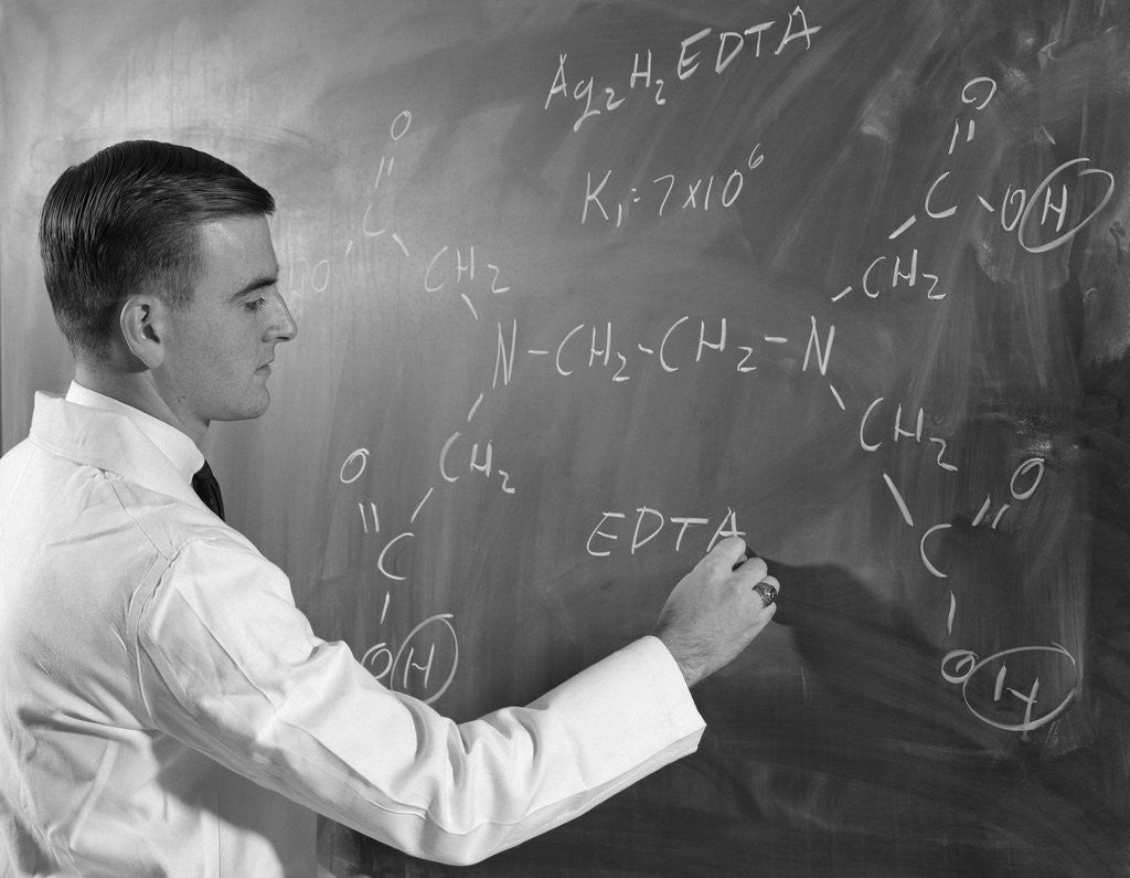 Detail of 1960s Profile Of Scientist Man In Lab Coat Writing Out Chemical Formula On Blackboard by Corbis