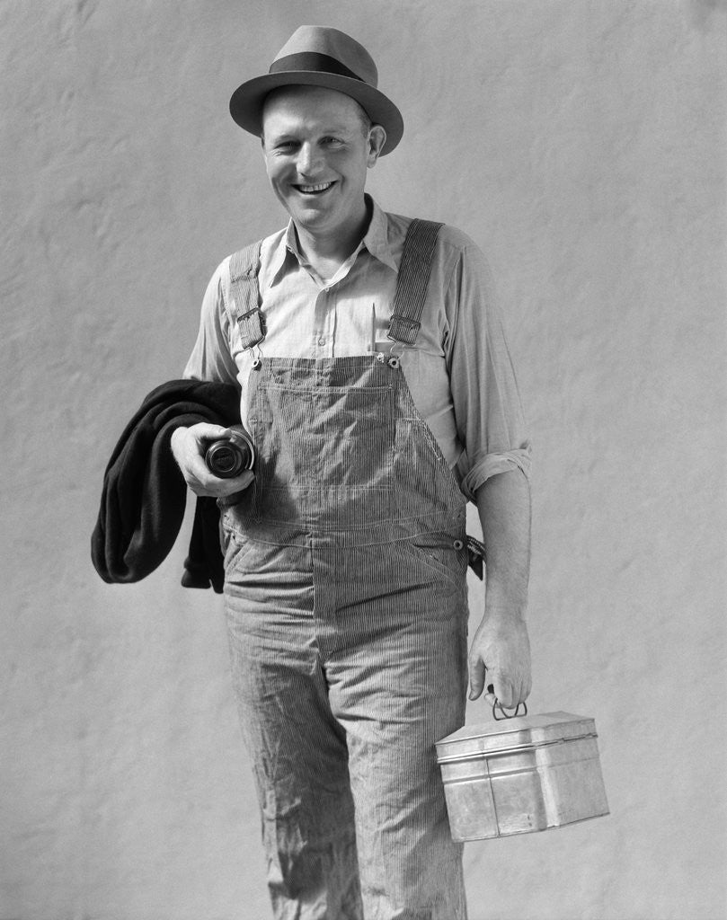 Detail of 1930s Man In Work Clothes Overalls Holding Lunch Box Thermos Bottle And Sweater by Corbis