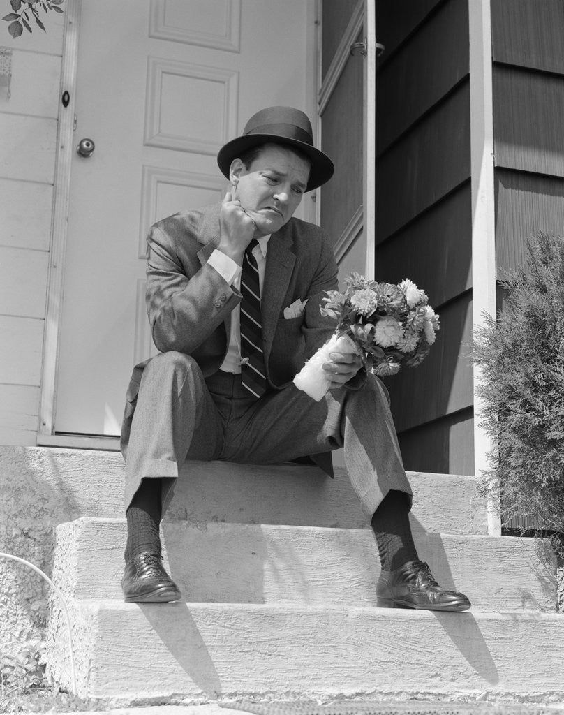 Detail of 1950s Man In Suit And Hat Holding Flowers Sitting Outside Front Door On Steps Looking Sad by Corbis