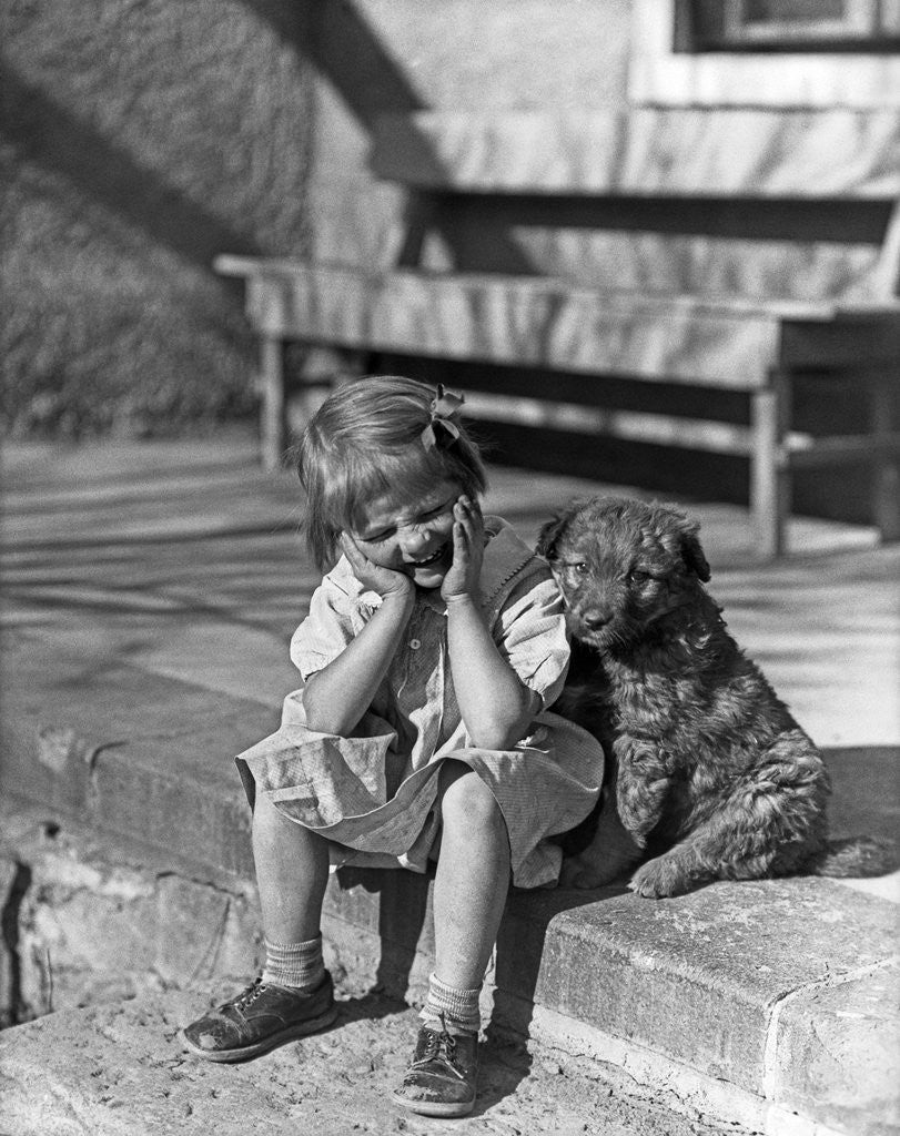 Detail of Little girl sitting on porch stoop funny expression hands up to her face beside her dog by Corbis