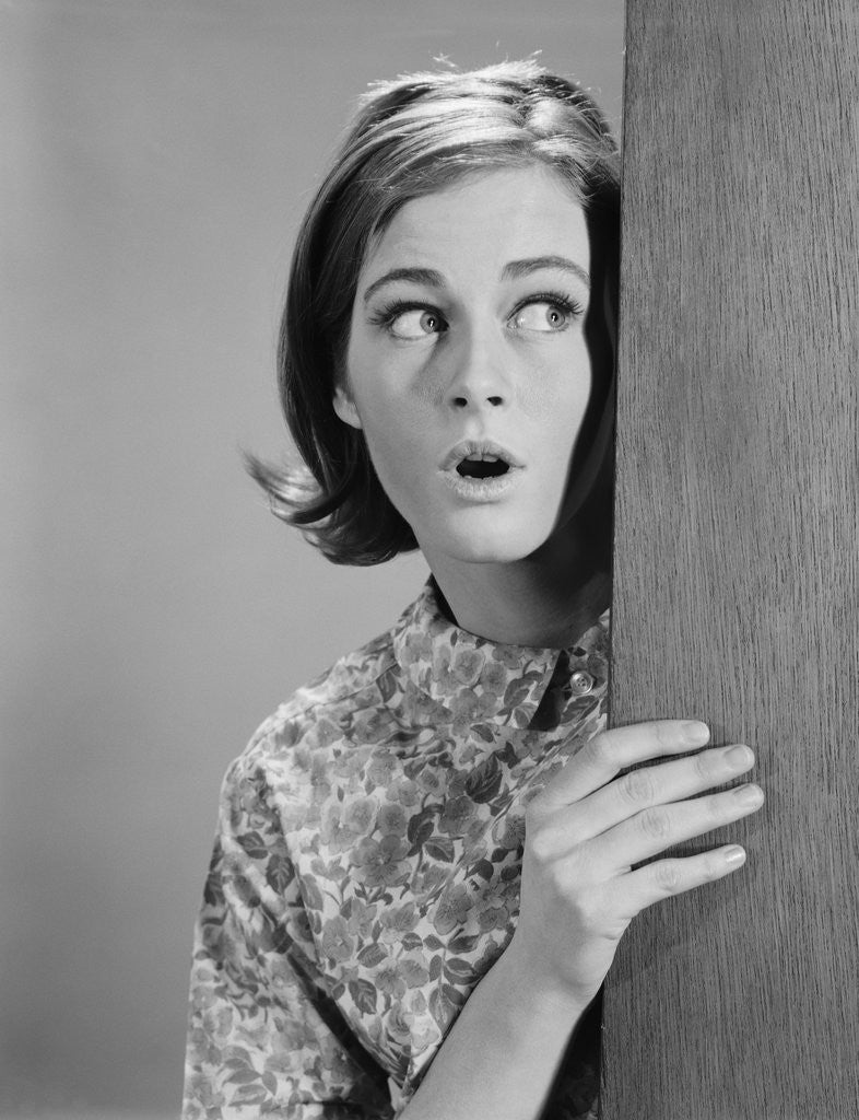 Detail of Woman peeking around door corner with fearful expression by Corbis