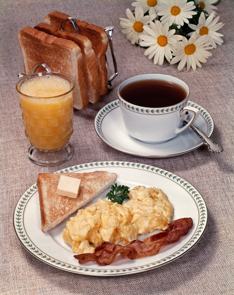 Detail of Scrambled eggs bacon toast on dish glass orange juice toast in rack cup of coffee daisies breakfast by Corbis