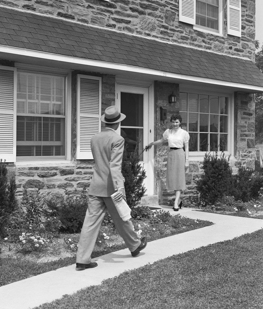 Detail of Man coming home down sidewalk woman waiting at door by Corbis