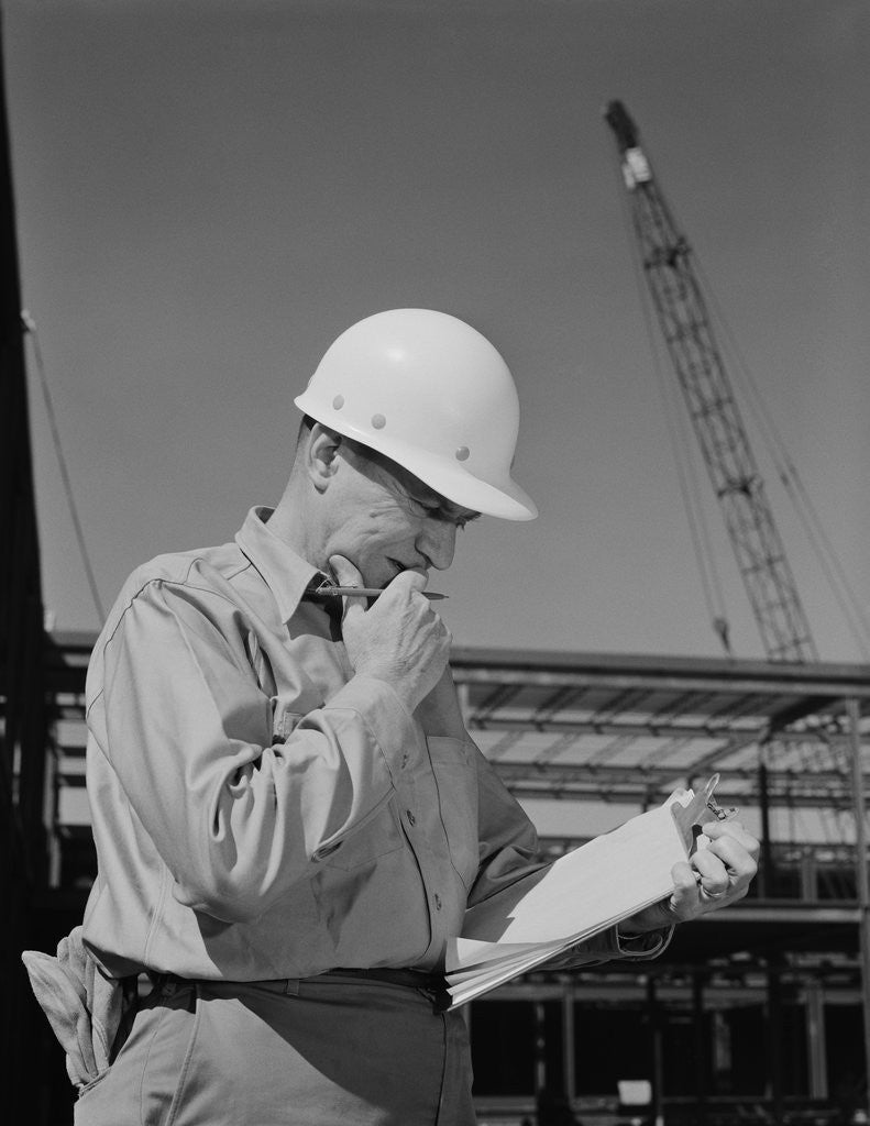 Detail of Male construction site supervisor wearing hard hat reading papers by Corbis