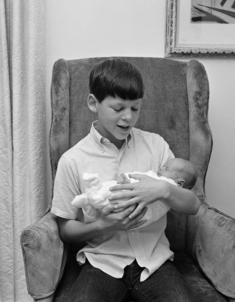 Detail of 1960s pre-teen boy sitting in armchair holding infant newborn baby sibling by Corbis