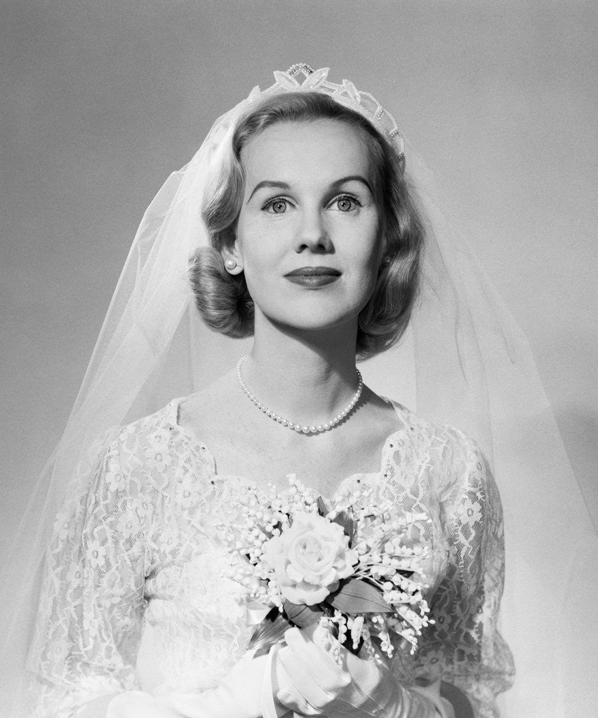 Detail of 1950s portrait woman bride pearl necklace white gloves holding small bouquet looking at camera by Corbis