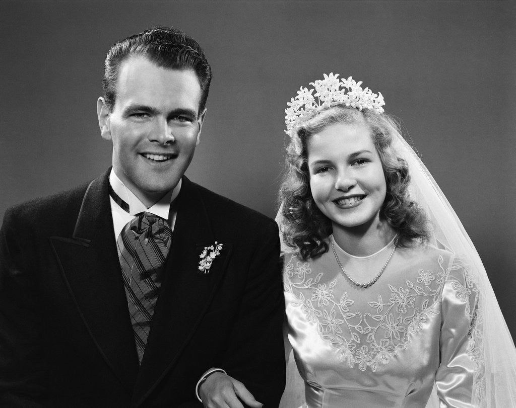 Detail of 1940s portrait of bride and groom linked arm in arm looking at camera by Corbis