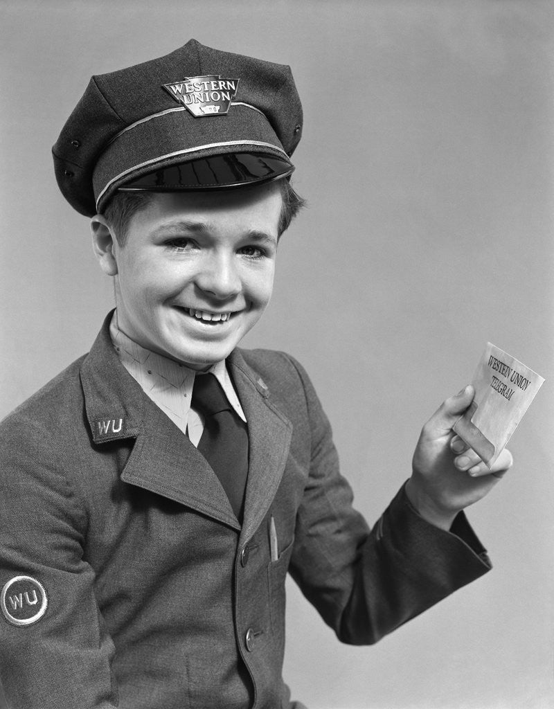 Detail of 1920s 1930s 1940s smiling boy wearing a western union uniform and hat holding a telegram looking at camera by Corbis