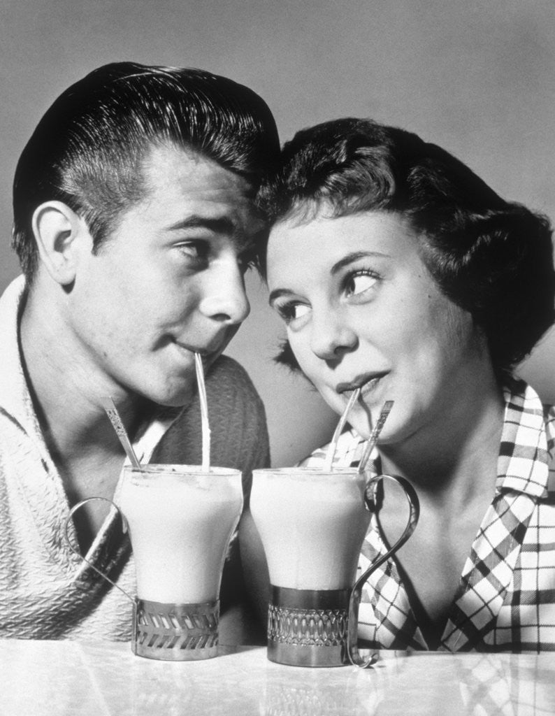 Detail of 1940s 1950s romantic teenage couple boy and girl head to head drinking ice cream sodas by Corbis