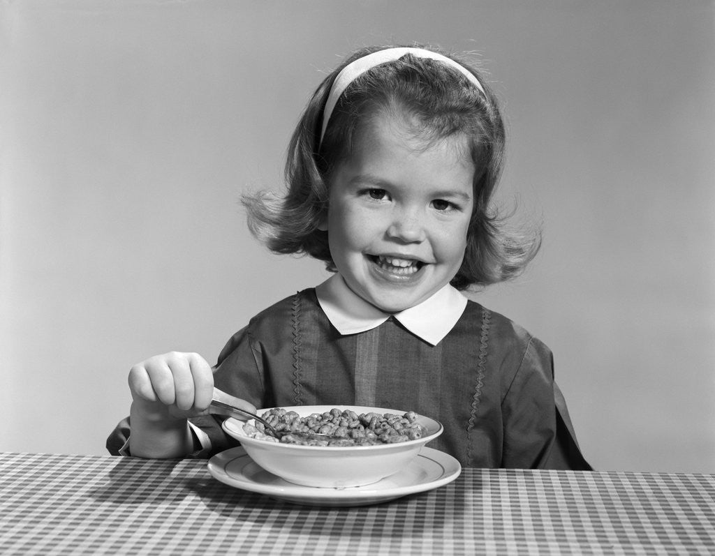 Detail of 1950s 1960s smiling little girl eating a bowl of breakfast cereal looking at camera by Corbis