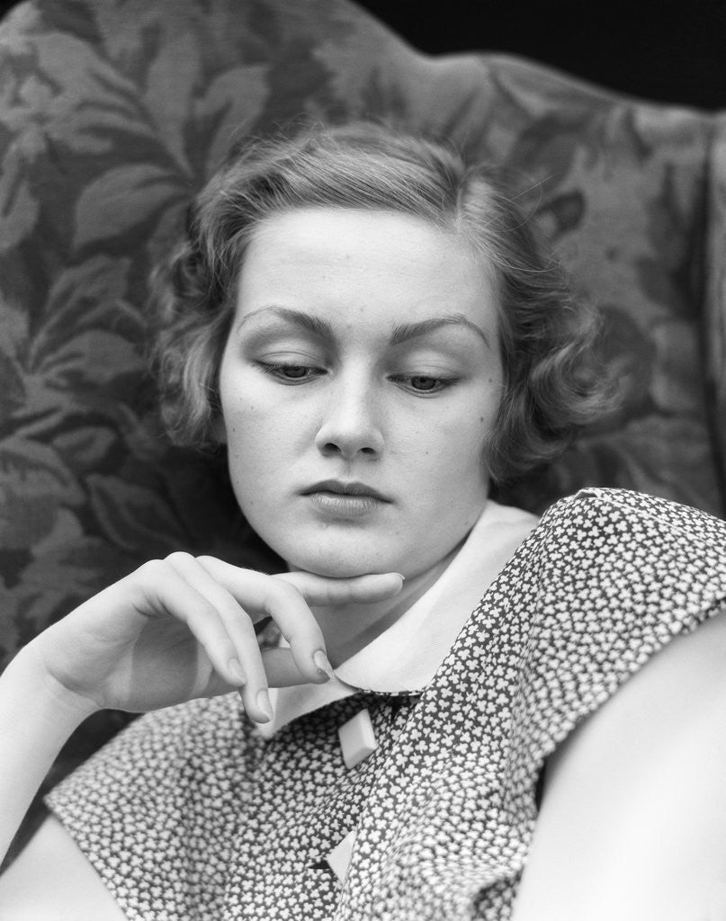 Detail of 1930s portrait of woman looking down with sad expression and her chin resting on index finger by Corbis