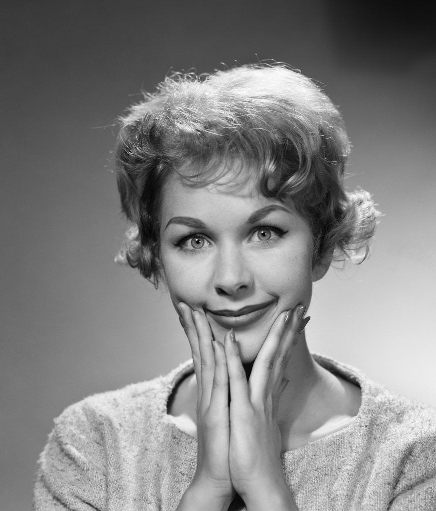 Detail of 1950s 1960s happy bemused woman facial expression both hands to chin smile looking at camera by Corbis