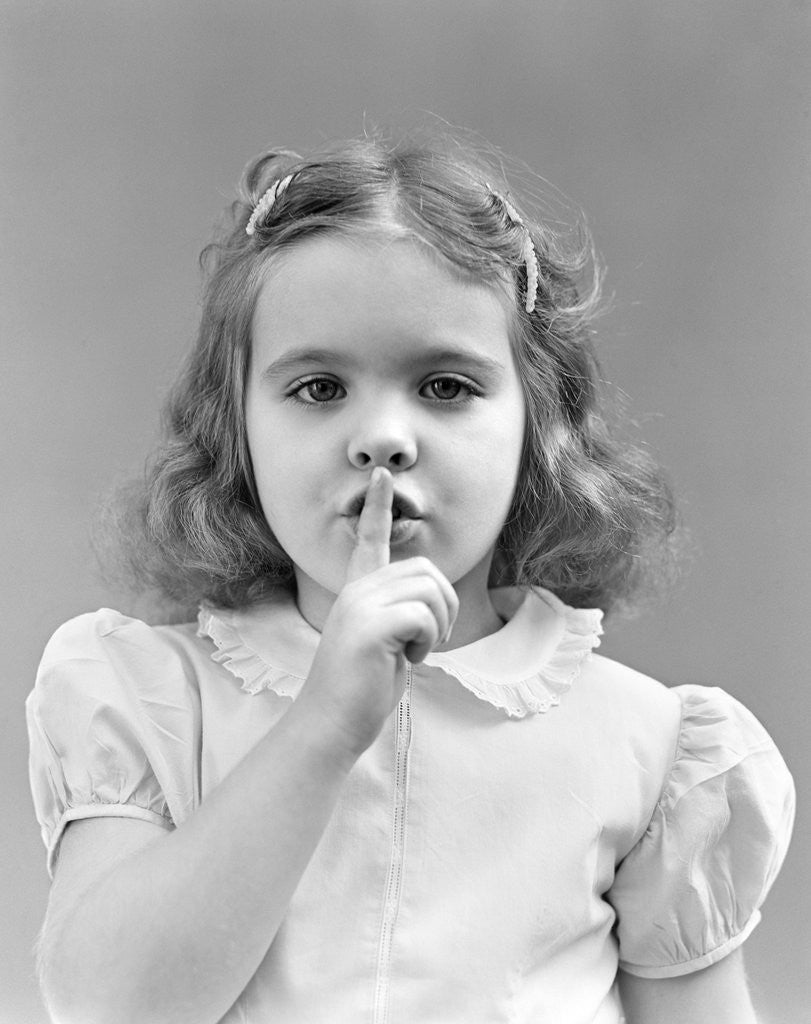 Detail of 1940s 1950s girl with finger to lips making quiet shush gesture looking at camera by Corbis