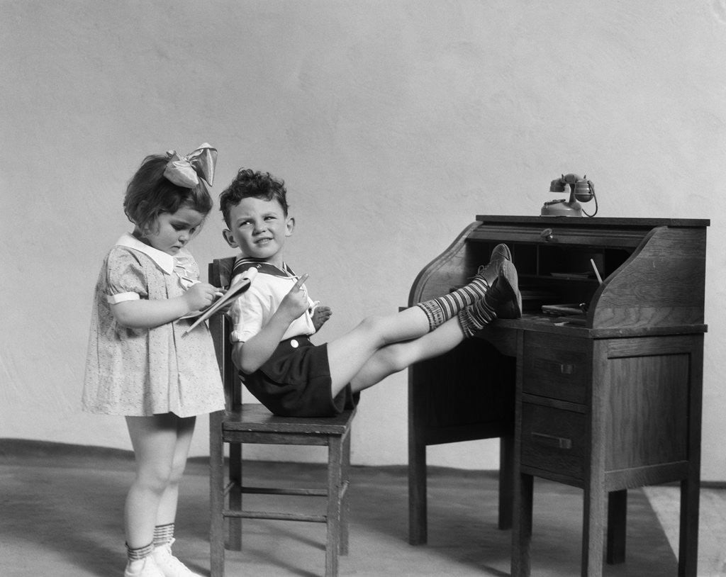 Detail of 1930s two children boy and girl playing office boss feet on desk secretary taking dictation by Corbis