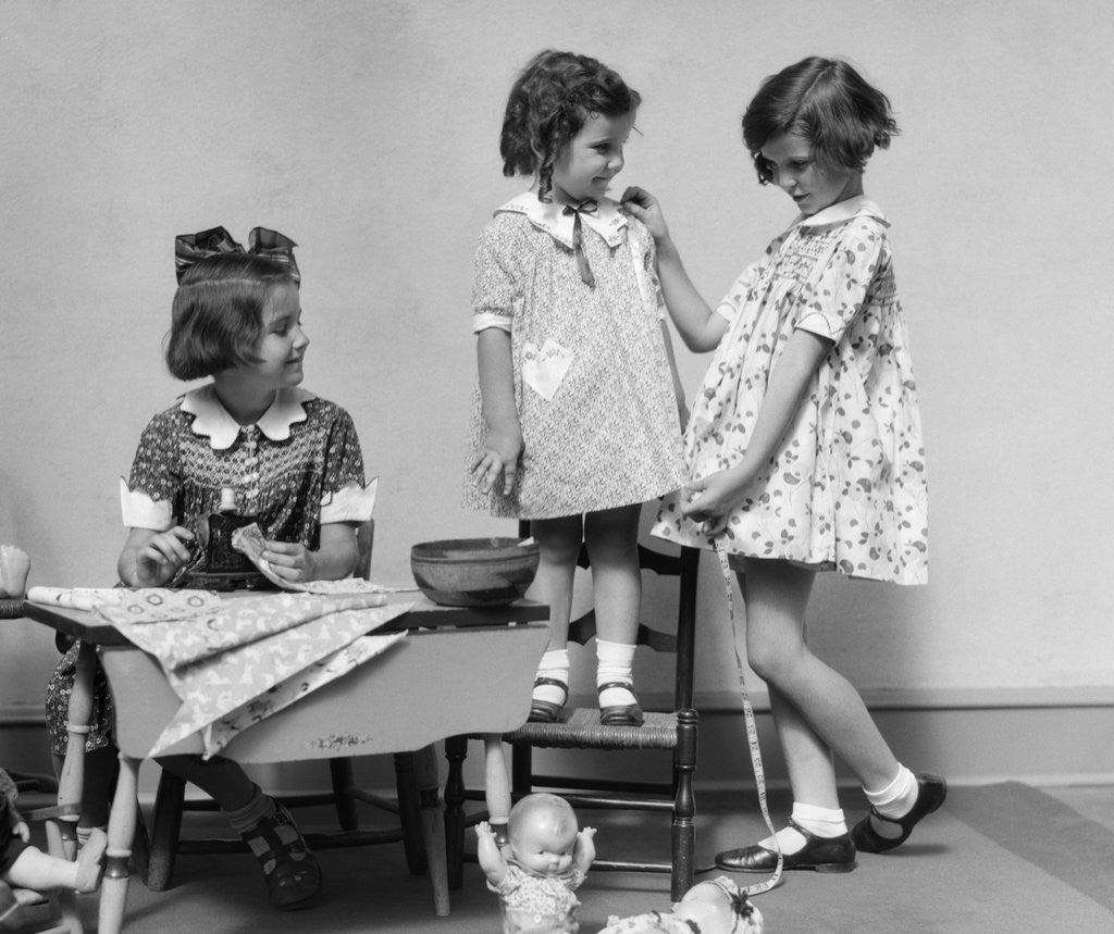 Detail of 1930s three girls playing fashion seamstress pretending measuring fabric by Corbis