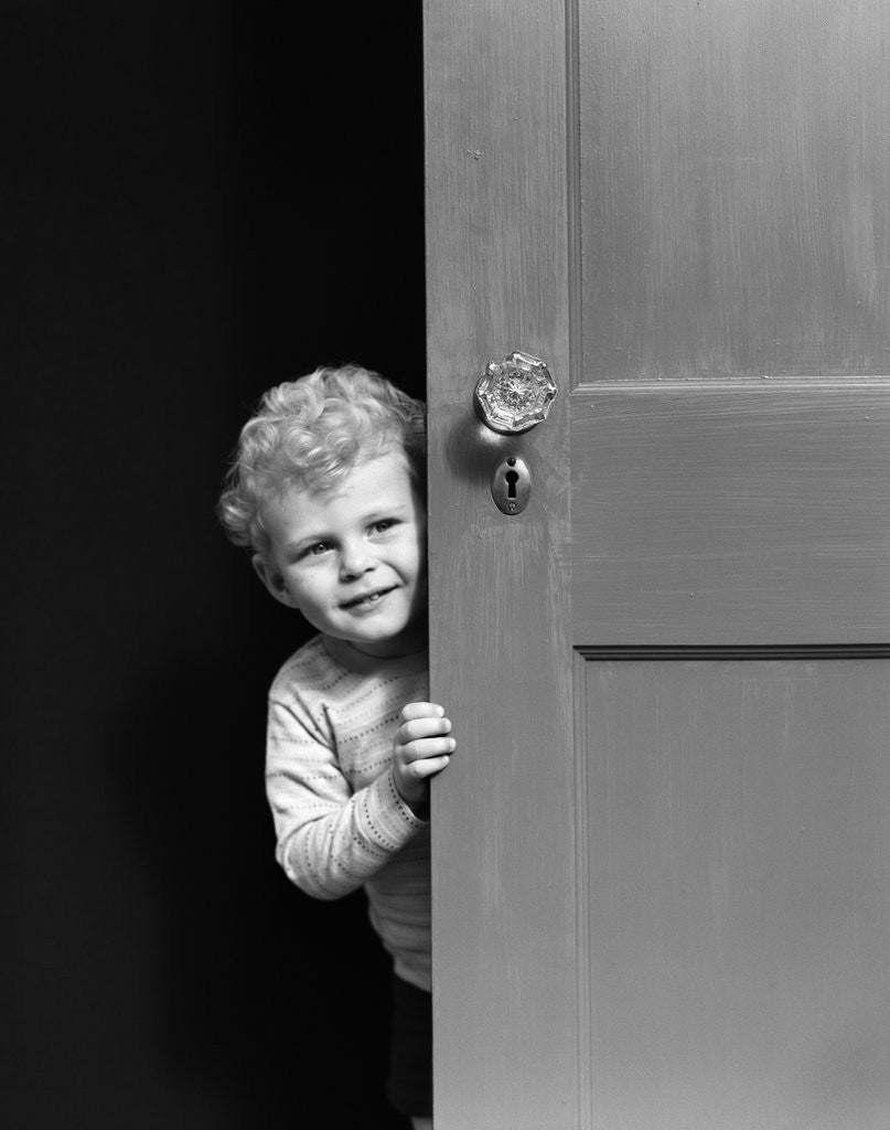 Detail of 1940s child little boy peeking looking around door by Corbis