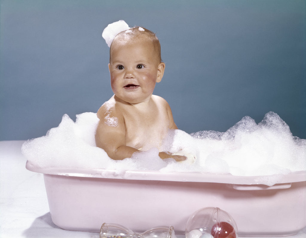 Detail of 1960s smiling baby sitting in bathtub bubble bath covered with soap bubbles by Corbis