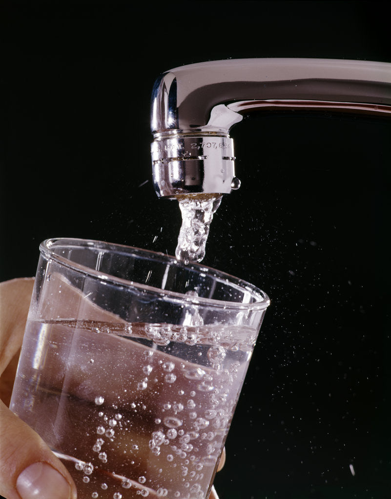 Detail of 1970s hand holding glass under faucet filling with drinking water by Corbis