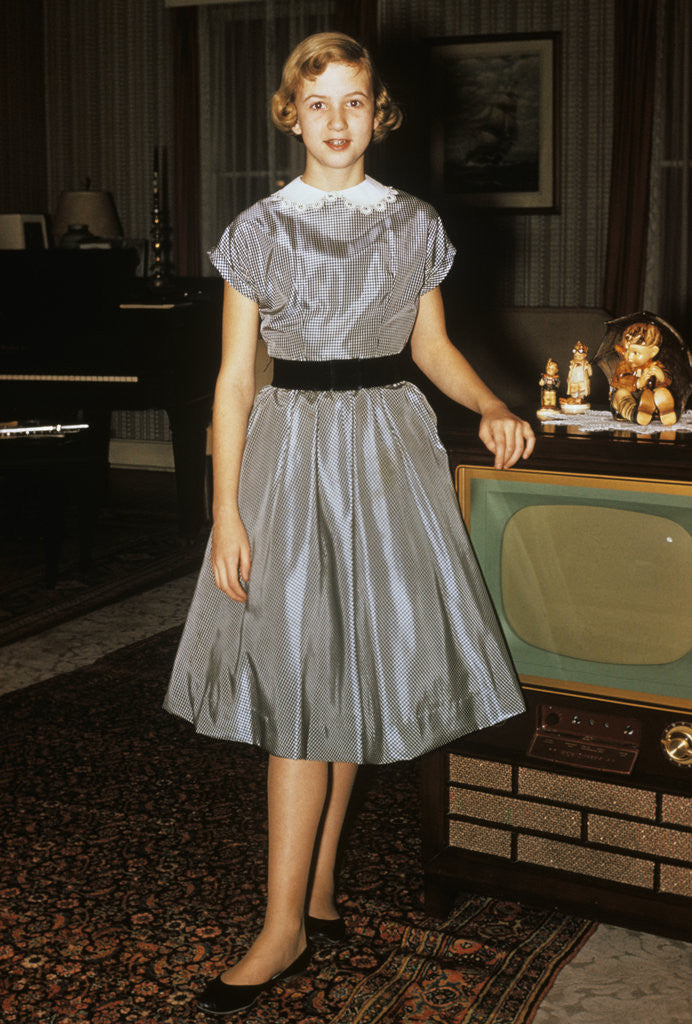 Detail of 1950s teenage girl dressed for her first date in gray silky dress posed by television set by Corbis