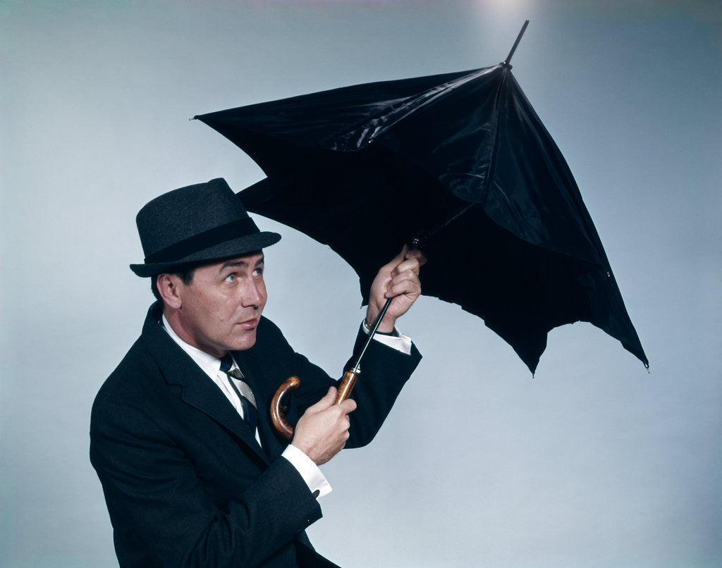 Detail of 1960s businessman wearing hat opening umbrella to protect from rain by Corbis