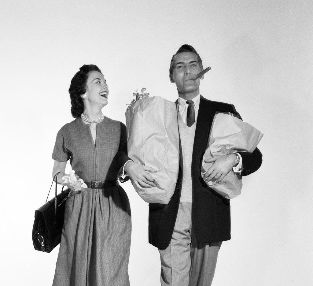 Detail of 1950s couple walking woman smiling at man carrying grocery bags smoking cigar by Corbis