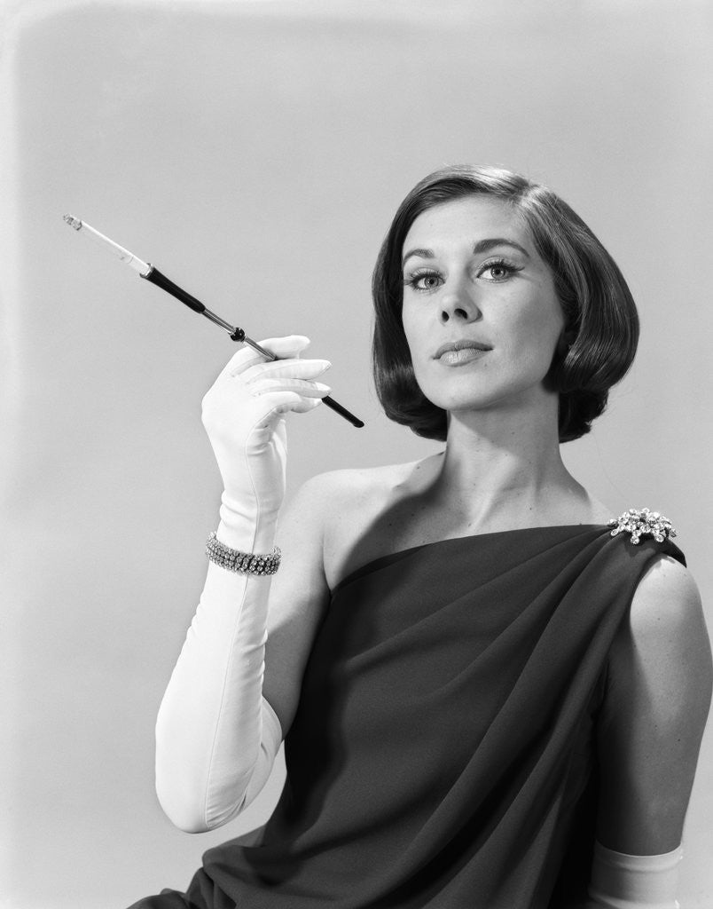 Detail of 1960s formally elegantly dressed young woman arrogant expression holding long cigarette holder wearing long white gloves by Corbis