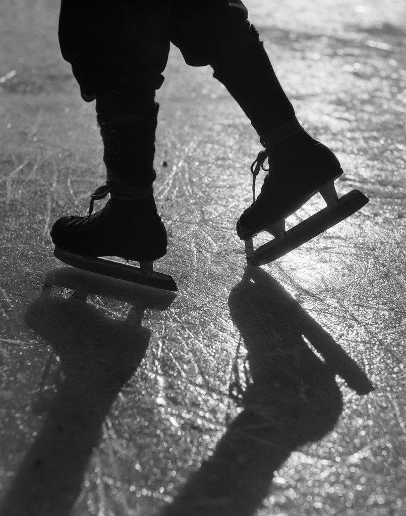 Detail of 1930s silhouette figure shown from knees down wearing ice skates skating in ice sun glare by Corbis