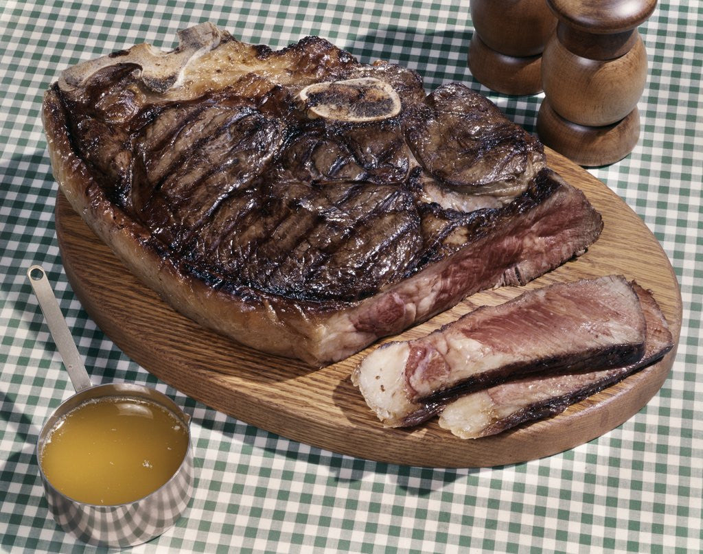 Detail of 1960s Huge Porterhouse Steak On Wooden Platter Sliced Medium Rare Cup Of Drawn Butter Salt Pepper Shakers Green Checked Cloth by Corbis