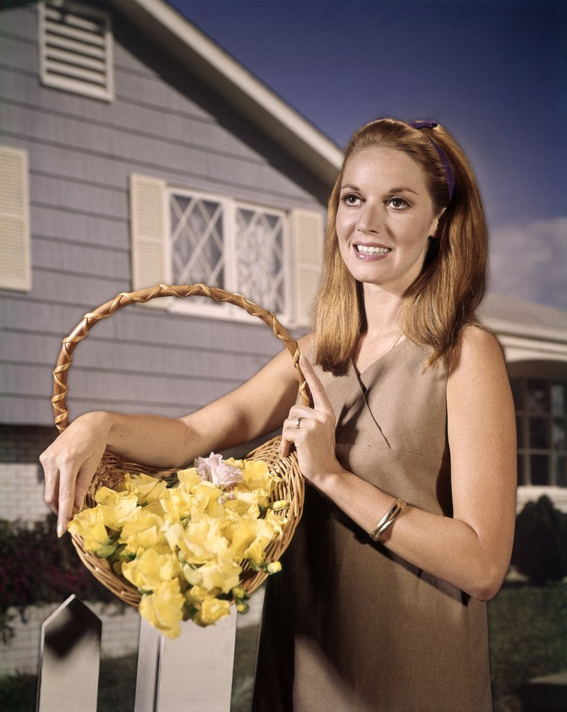 Detail of 1960s Smiling Woman Holding Basket Yellow Flowers House Background by Corbis