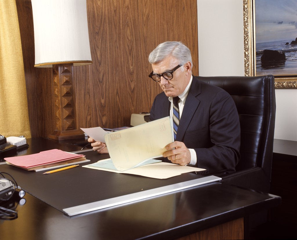 Detail of 1960 1960s 1970 1970s Mature Man Silver Gray Grey Hair Executive Seated Desk Reading Business Papers Men Executives by Corbis