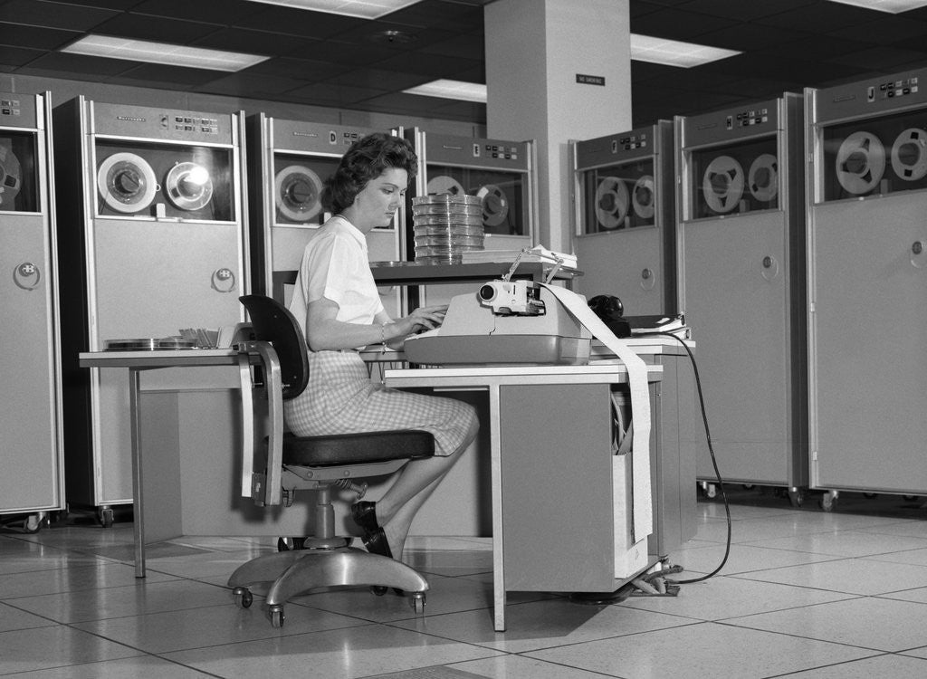 Detail of 1960s Woman In Mainframe Computer Room Surrounded By Many Data Tape Drives Sitting At Desk Typing On Typewriter Indoor by Corbis