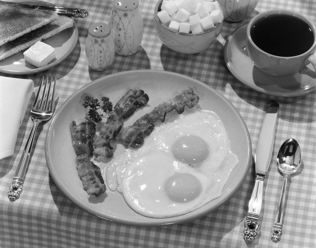 Detail of 1950s Breakfast Plate Of Bacon & Fried Eggs & Coffee Sugar Bowl Toast Salt & Pepper Shakers On Checkered Tablecloth by Corbis