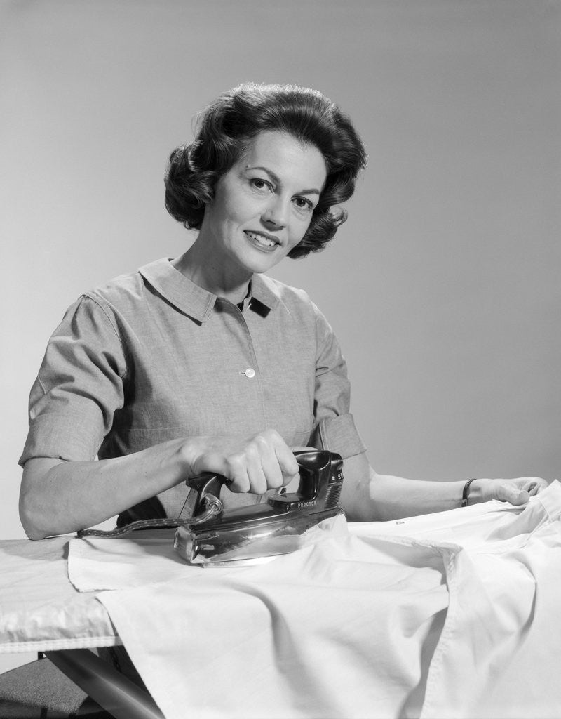 Detail of 1950s Smiling Woman Housewife Ironing Shirt Looking At Camera by Corbis