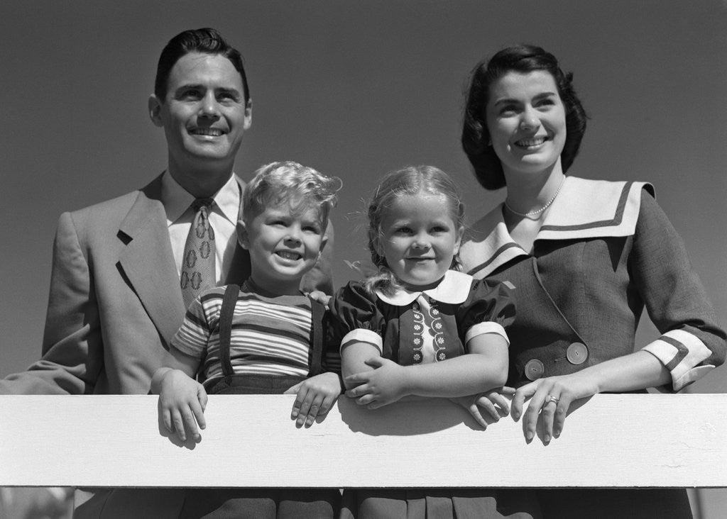 Detail of 1950s Portrait Smiling Family Father Mother Daughter Son Standing Together Behind White Fence Outdoor by Corbis