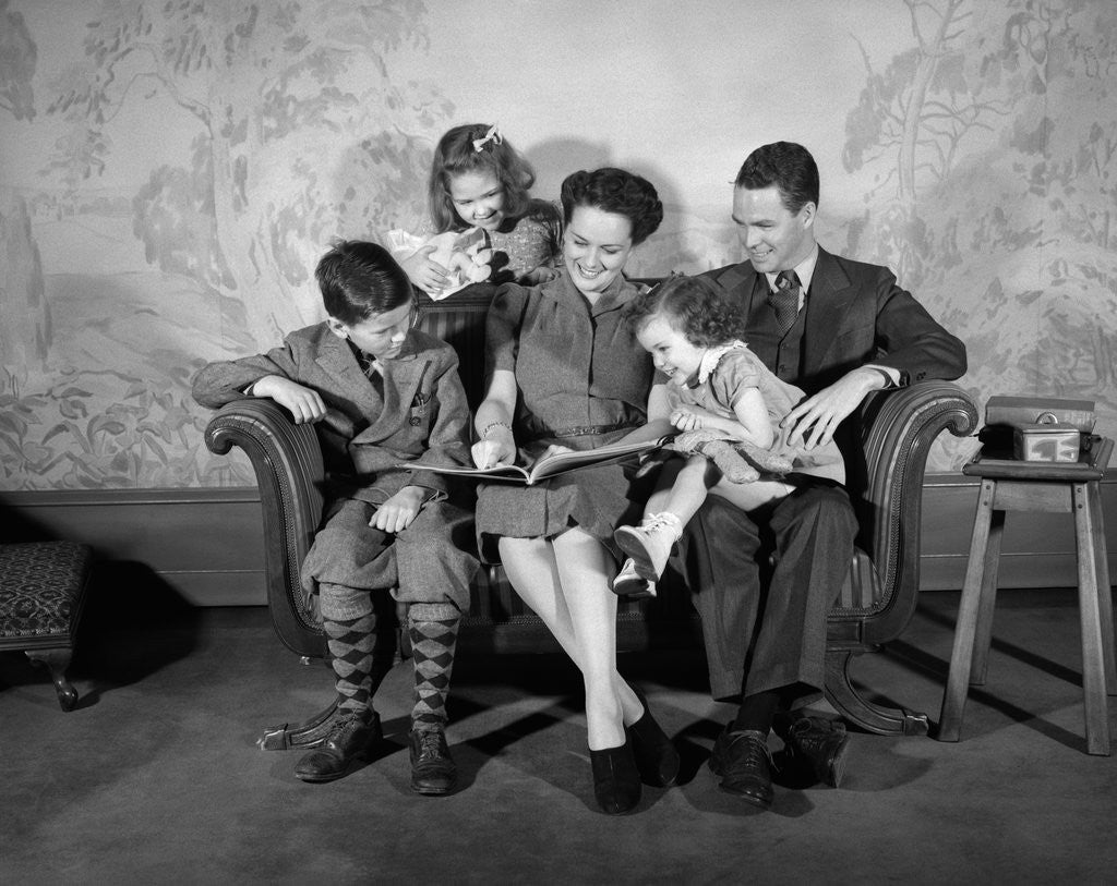 Detail of 1930s 1940s Family Sitting On Couch Looking Reading Book Together by Corbis