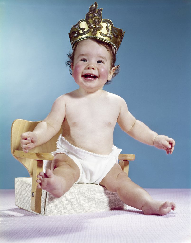 Detail of 1960s Smiling Happy Baby Wearing Crown Sitting On Booster Seat Chair Throne Looking At Camera by Corbis