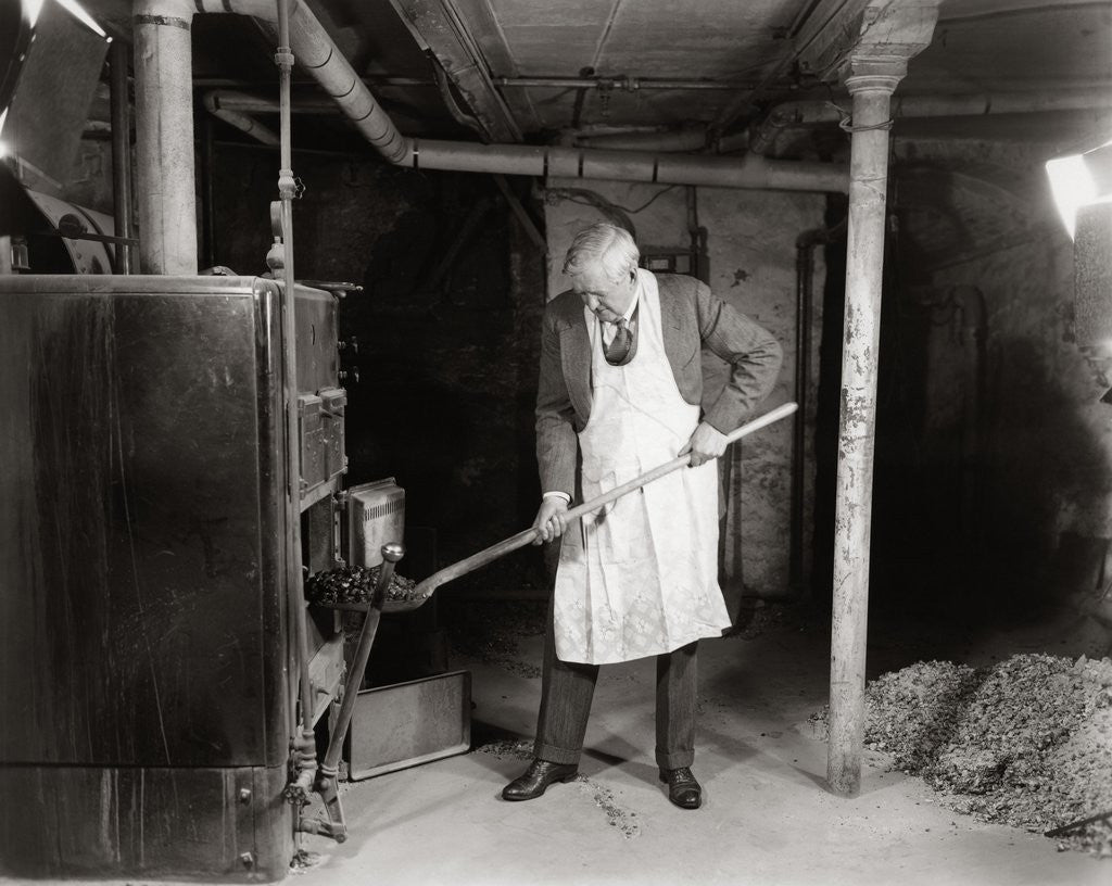 Detail of 1940s elderly man shoveling coal into furnace in a basement by Corbis