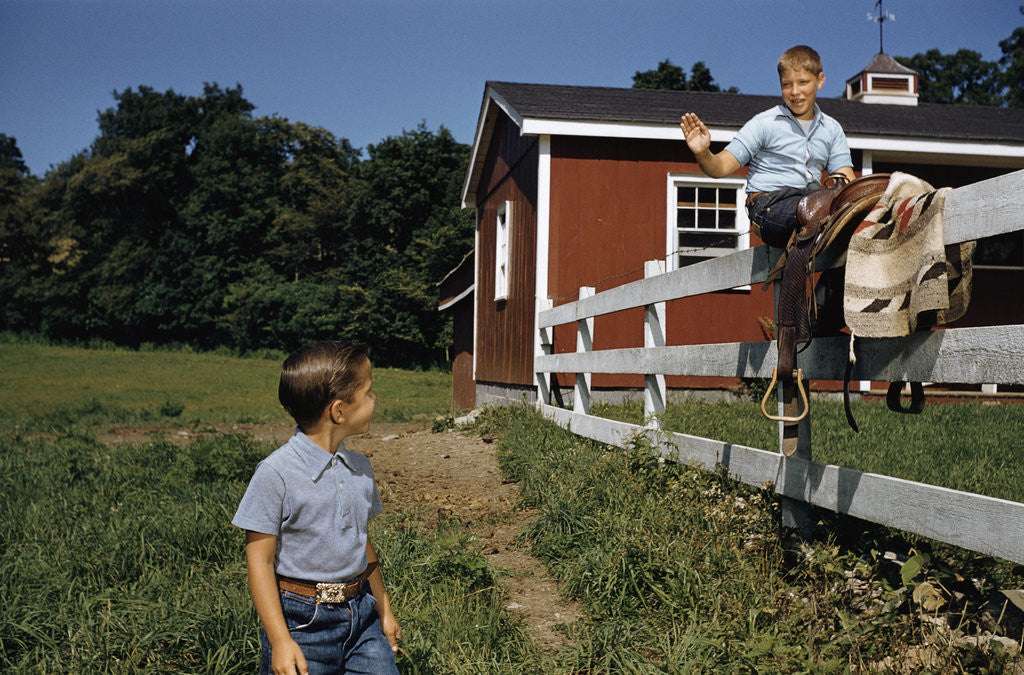 Detail of Boy Sitting on Fence Waving to Friend by Corbis